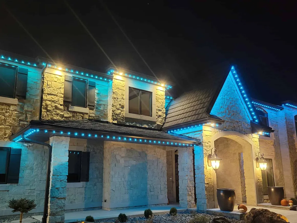 Stone home with vivid blue roofline lighting and warm entry lights