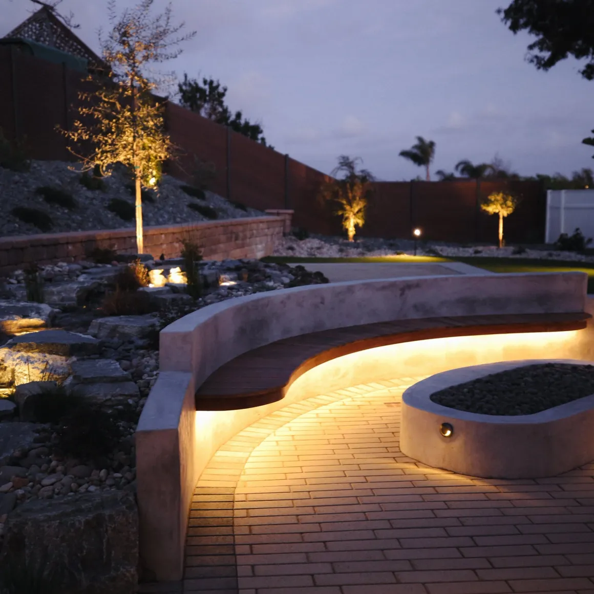 Dusk landscape lighting on paths, trees, and a retaining wall
